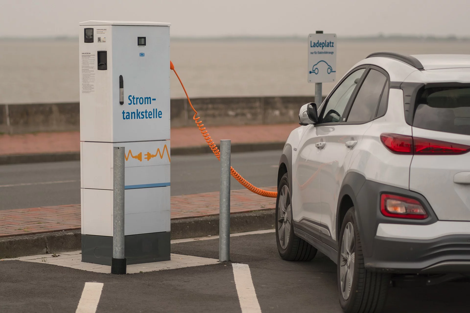 E-Ladesäule, daneben Rückansicht eines ladenden Fahrzeugs