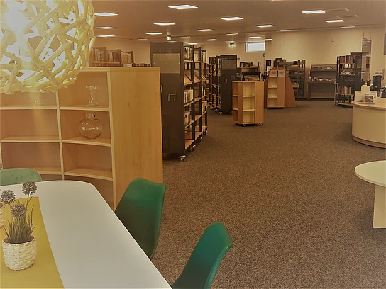 Blick in das Foyer der Bücherei mit hözernen mit Büchern gefüllten Regalelementen Ecke Tisch mit Blick in die Stadtbücherei