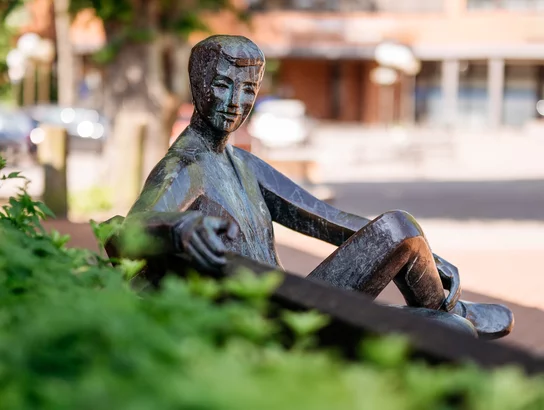 Bronzefigur mit einladender Handbewegung auf Bank