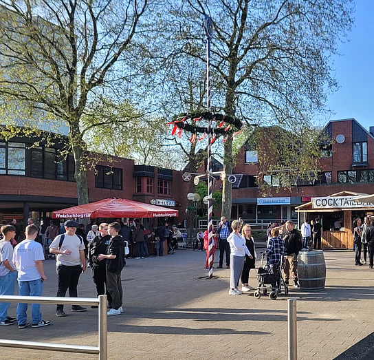 Menschen zwischen Buden und Maibaum auf dem Marktplatz Wahlstedt
