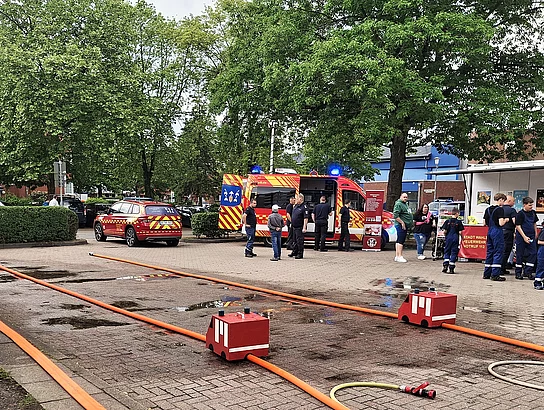 Schläuche auf dem Pflaster, dahinter Feuerwehrwagen und Menschen in Feuerwehrkleidung